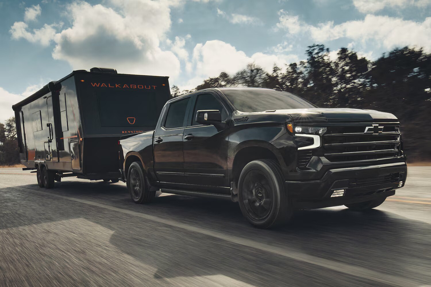 A black Chevrolet Silverado 1500 towing a black Walkabout trailer as it drives on the road A black Chevrolet Silverado 1500 towing a black Walkabout trailer as it drives on the road
