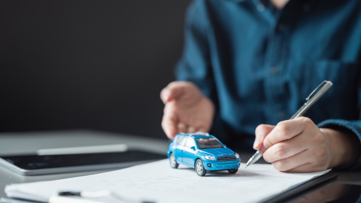 A person working on vehicle financing paperwork with a blue, toy car on it A person working on vehicle financing paperwork with a blue, toy car on it