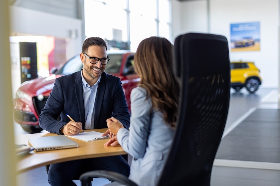 A car dealer discussing paperwork with a customer inside a car dealership