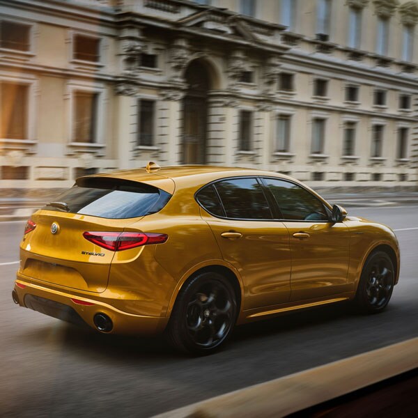 Golden Alfa Romeo Stelvio driving in European city from the rear.