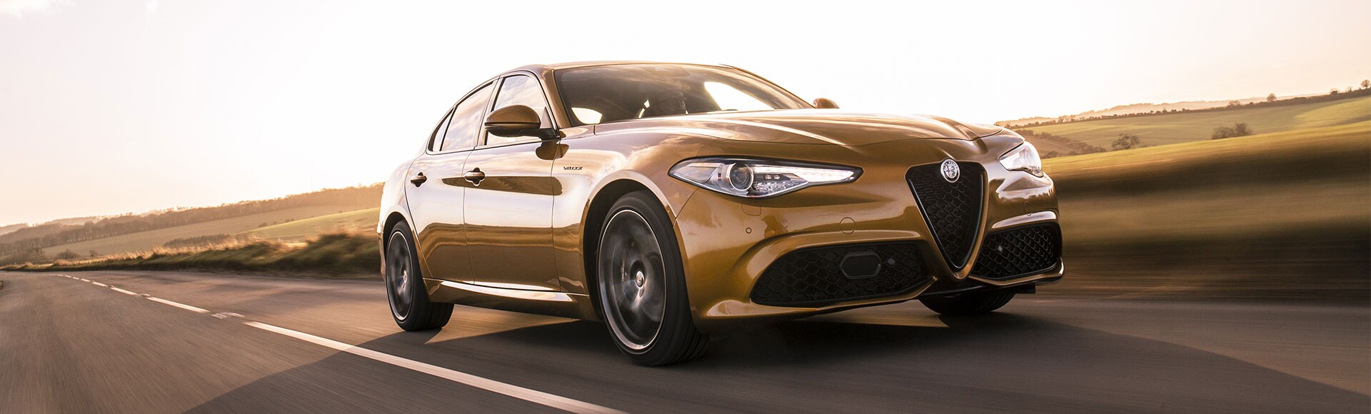 Sunlit Alfa Romeo Giulia driving on a country road.
