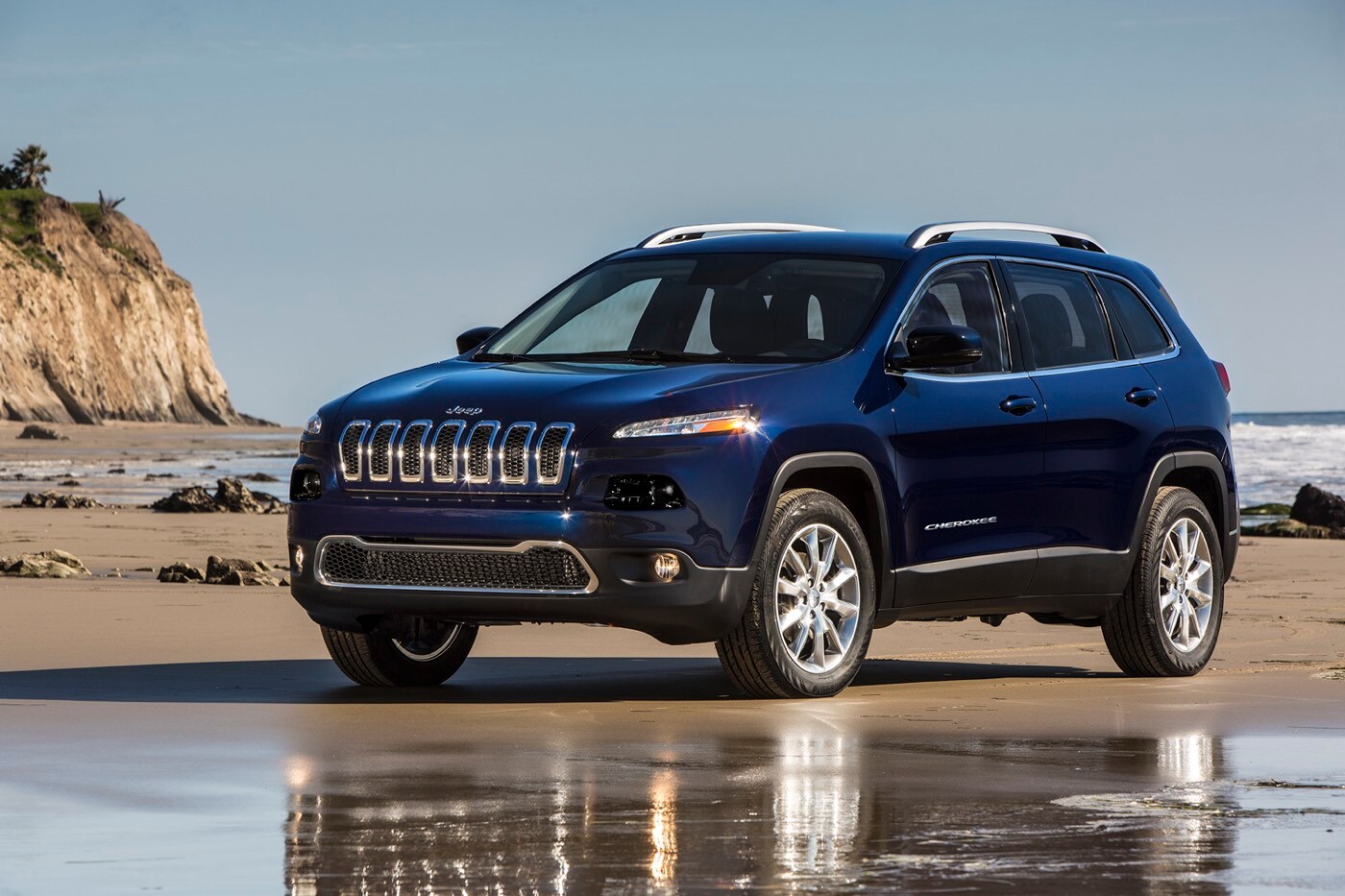 Vue 3/4 avant d'un VUS Jeep Cherokee Limited 2016 bleu garé sur une plage