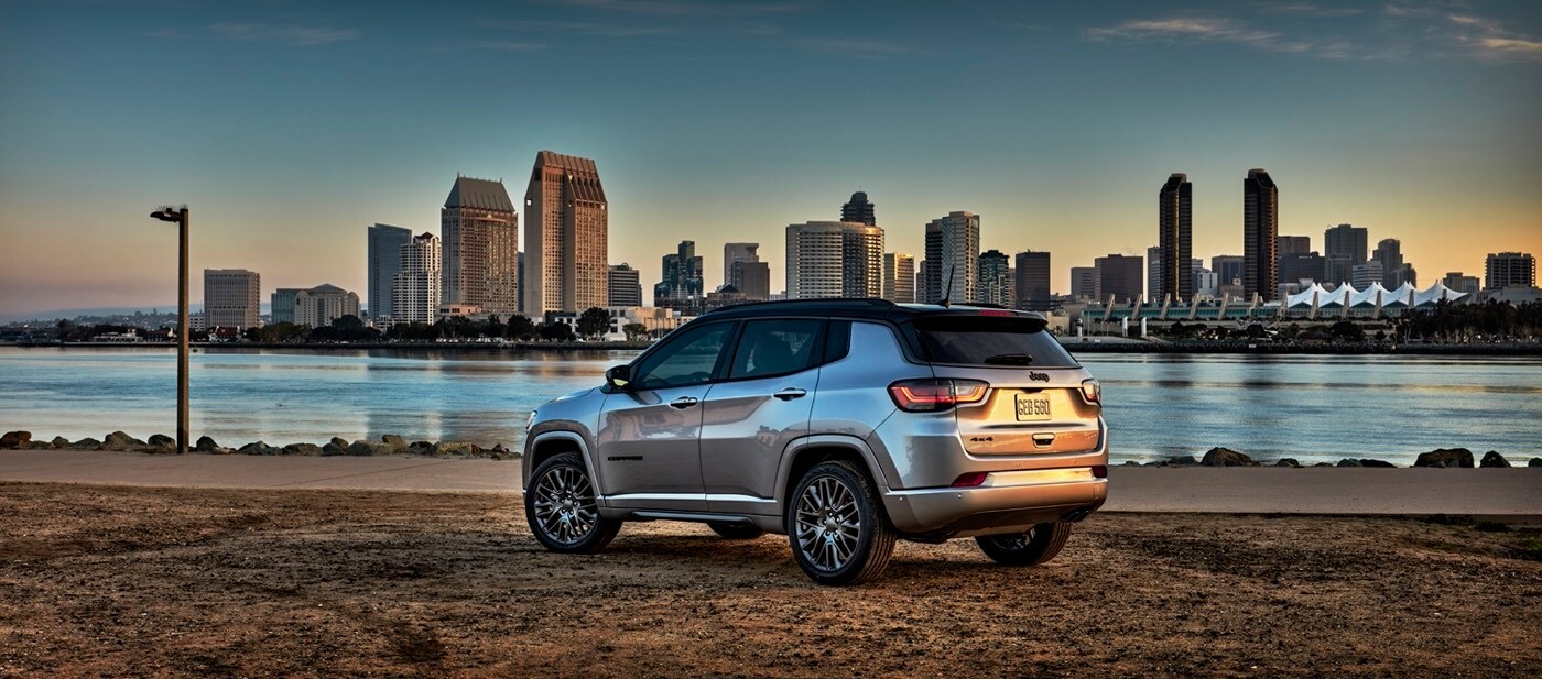 Vue latérale-arrière du Jeep Compass High Altitude 2022 garé au bord d'un fleuve avec une ville métropolitaine en arrière-plan