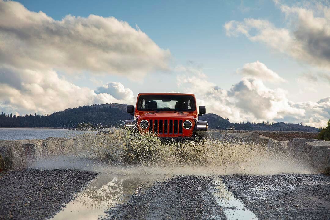Vue avant d'un Jeep Wrangler Rubicon 2021 rouge éclaboussant l'eau sur une piste bouetteuse