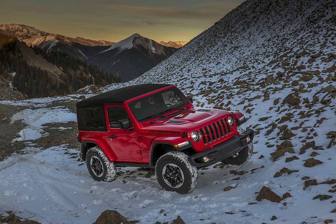 Vue 3/4 avant d'un Jeep Wrangler Rubicon 2021 rouge au bas d'une montagne enneigée incluant sa toiture souple