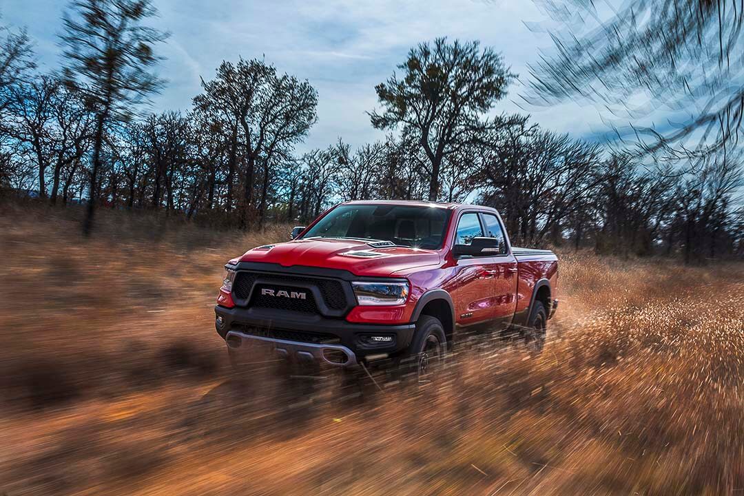 Vue 3/4 avant d'un RAM 1500 Rebel 2022 rouge roulant à travers les herbes en nature