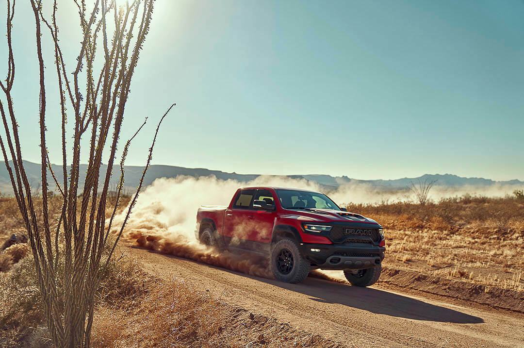 Un camion RAM 1500 TRX 2022 rouge dégageant un nuage de sable en roulant sur une route dans un désert
