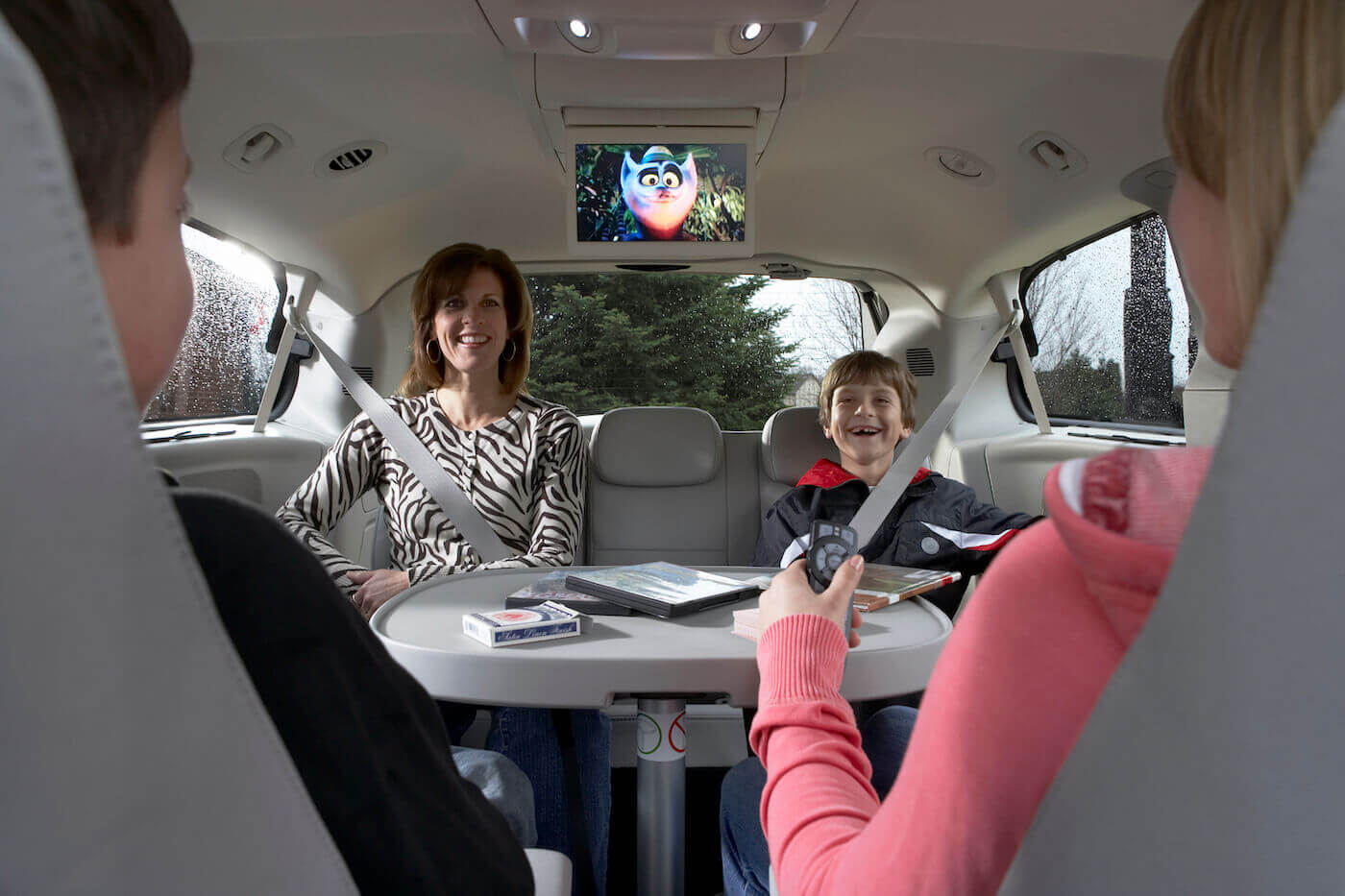 Famille heureuse jouant au carte, installée sur les sièges swivel'n Go d'un Dodge Grand Caravan 2010 avec le lecteur DVD au plafond