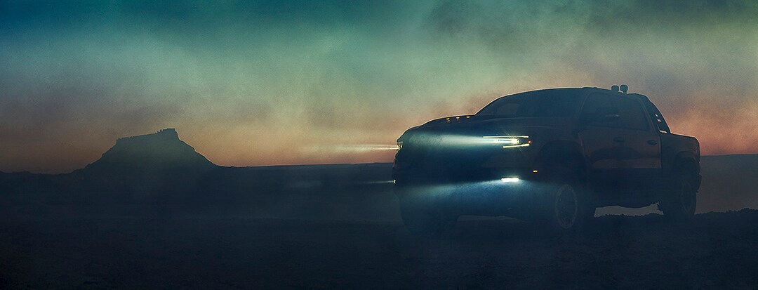 Un RAM 1500 TRX 2022 peu visible avec ses phares allumés parmi un nuage de poussière