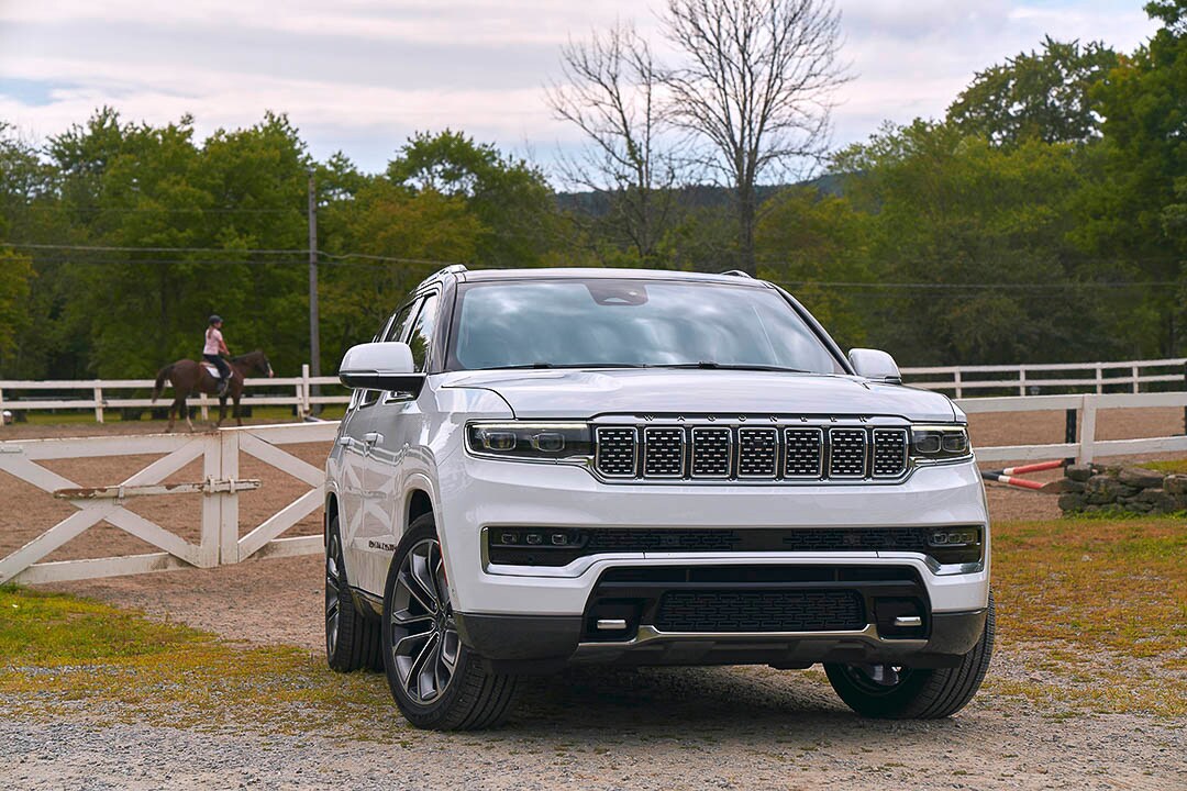 Vue 3/4 avant d'un Jeep Grand Wagoneer 2022 blanc éclatant garé à côté d'un enclos de cheval