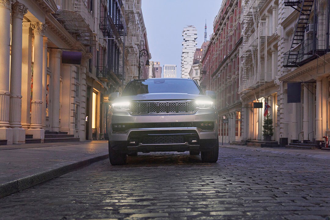 Vue avant d'un Jeep Grand Wagoneer 2022 zénith argenté avec ses phares allumés et garé sur un pavé