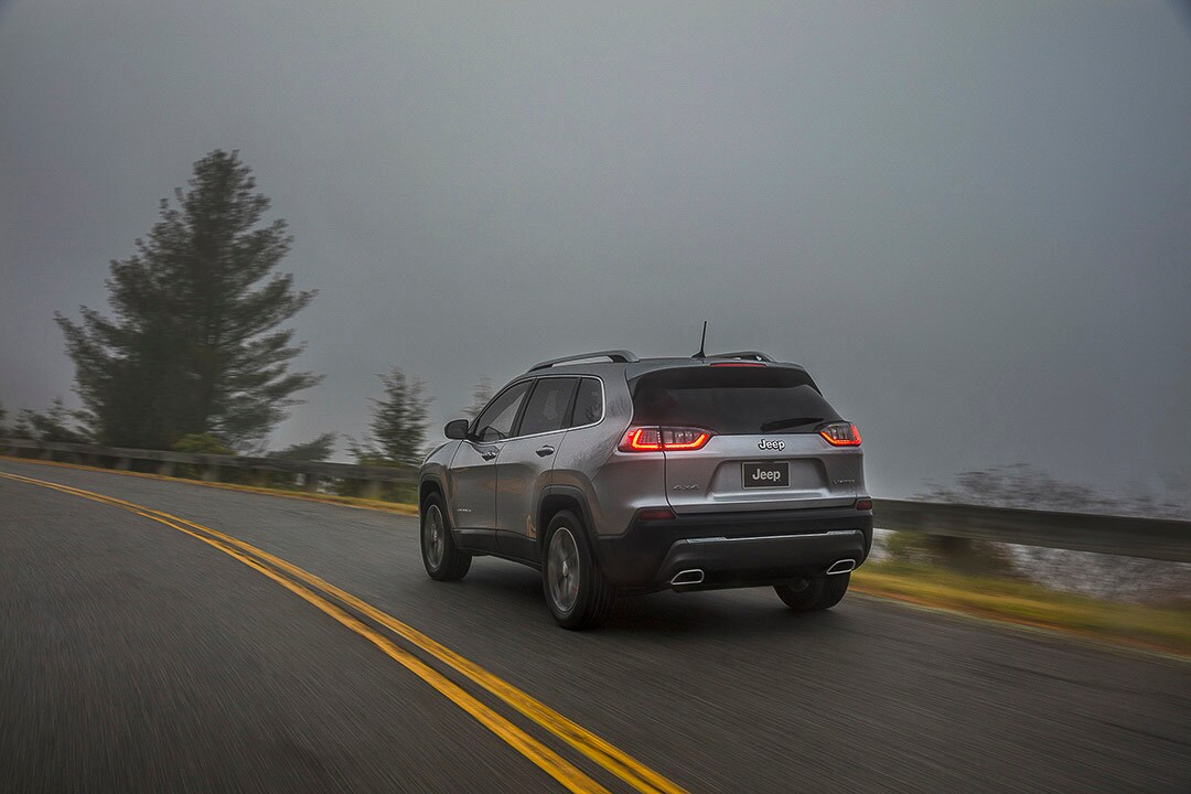 Dos et côté d'un Jeep Cherokee 2021 Limited argenté roulant en montagne brumeuse