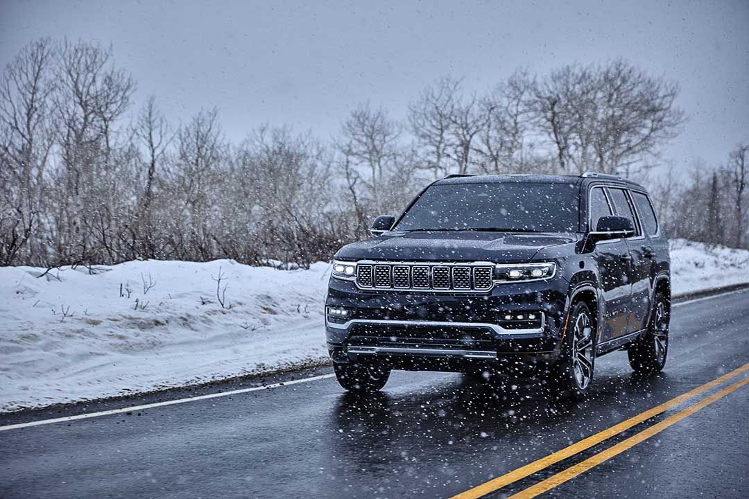 Vue 3/4 avant du Jeep Grand Wagoneer 2022 bleu roulant sur la route pendant qu'il neige