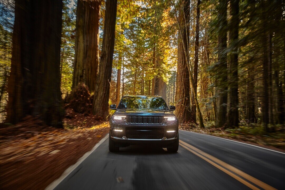 Vue avant du Jeep Grand Cherokee L Summit Reserve 2021 roulant sur une route entourée d'arbres