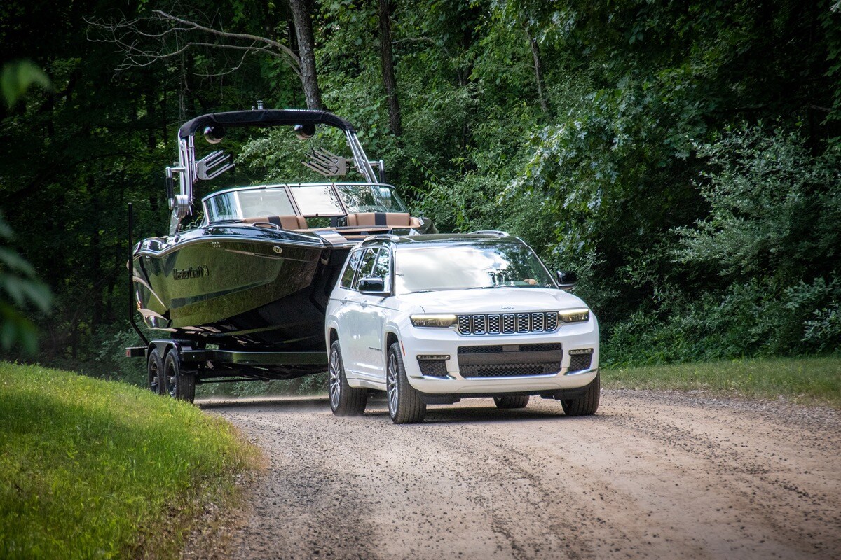 Le Jeep Grand Cherokee L Summit 2021 blanc remorquant un bateau sur une route en nature