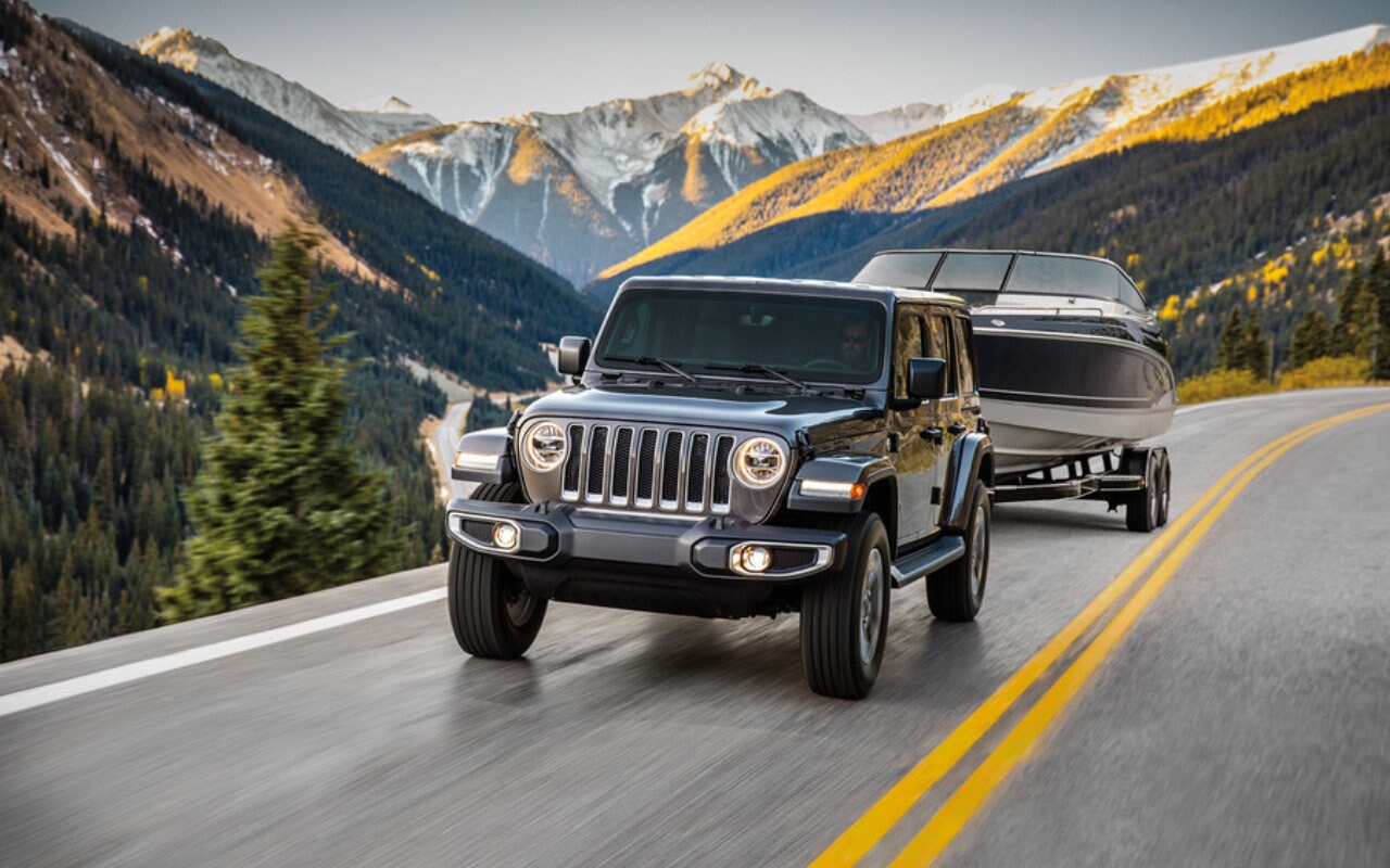 vue latérale avant d'un Jeep Wrangler 2023 qui traine un bateau sur une remorque sur une route de montagne