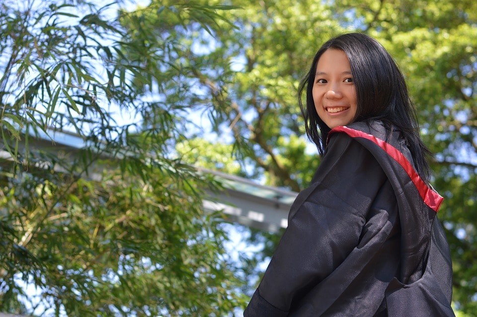 girl in black graduation gown with red trim outside trees in background.jpg
