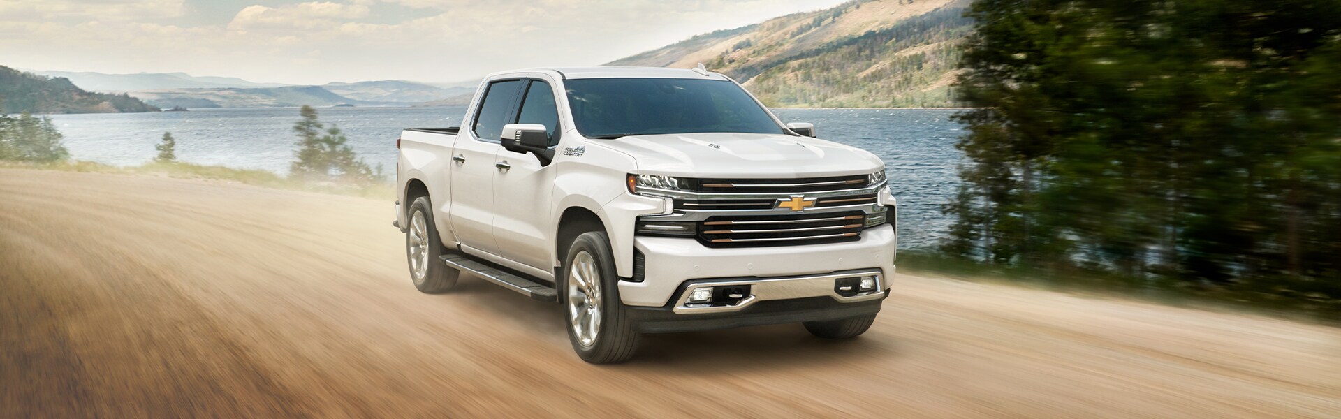 Chevrolet of New Bern is a Car Dealership in New Bern near Trent Woods NC | White 2020 Silverado Driving Down Dirt Road Next to Lake Chevrolet of New Bern is a Car Dealership in New Bern near Trent Woods NC | White 2020 Silverado Driving Down Dirt Road Next to Lake