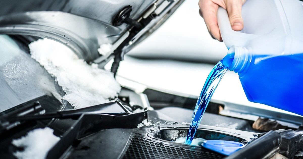 Technician adding antifreeze to a car with snow on it Technician adding antifreeze to a car with snow on it