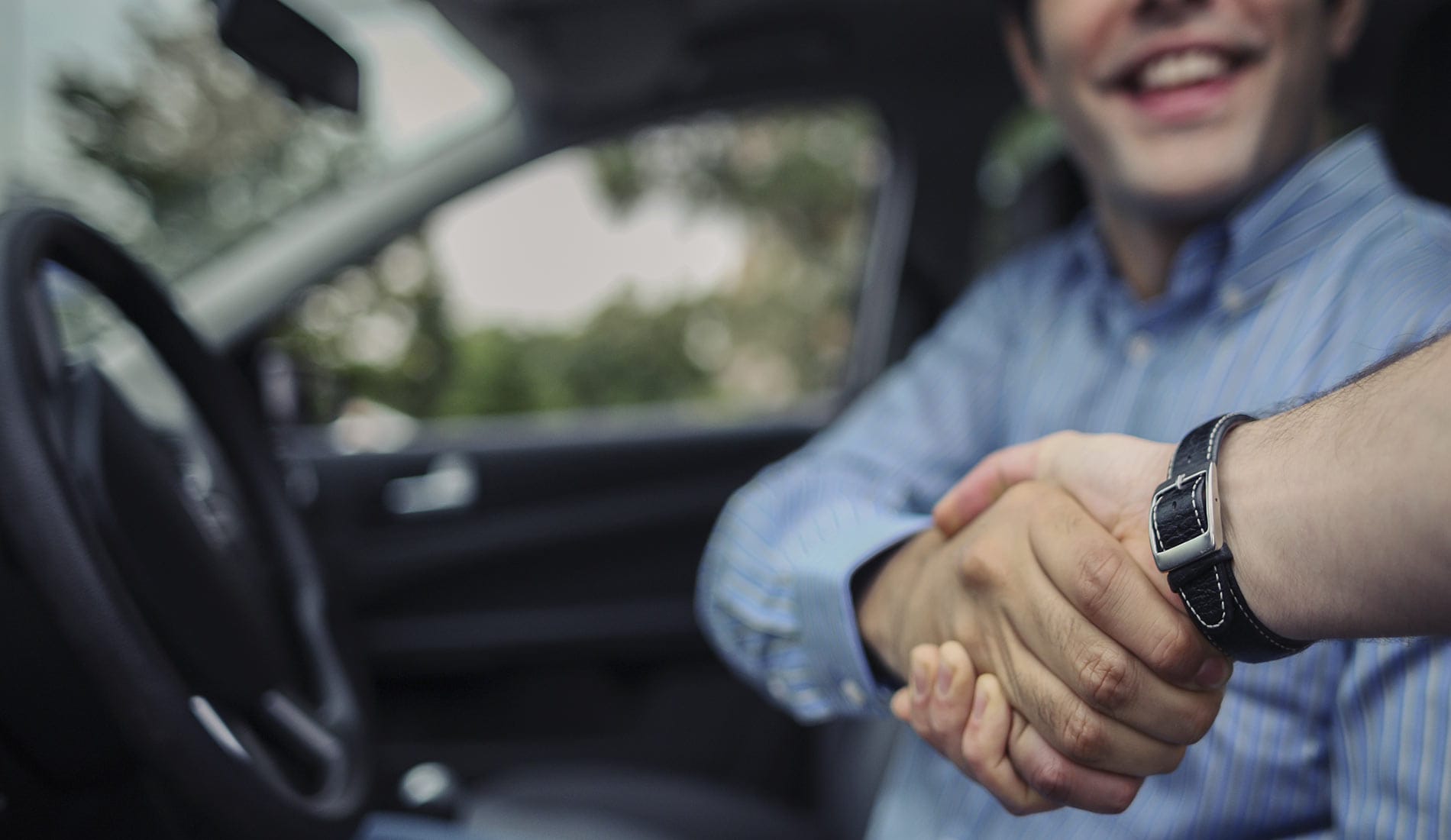 Used Dealership Near Niles, OH Young man happily shaking hands in his new used car