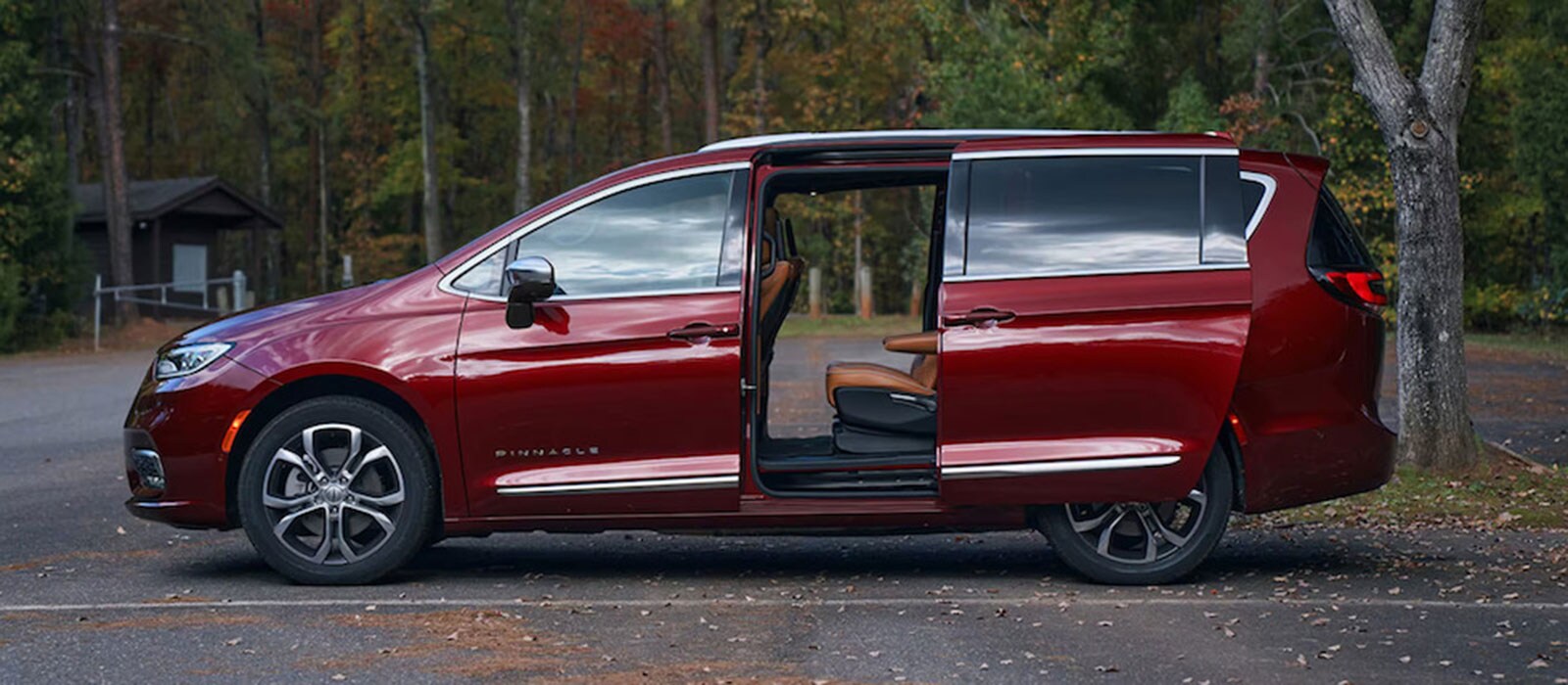 2026 Chrysler Pacifica Trim Level Comparison class= A red 2026 Chrysler minivan parked in a public park, with both its side doors open