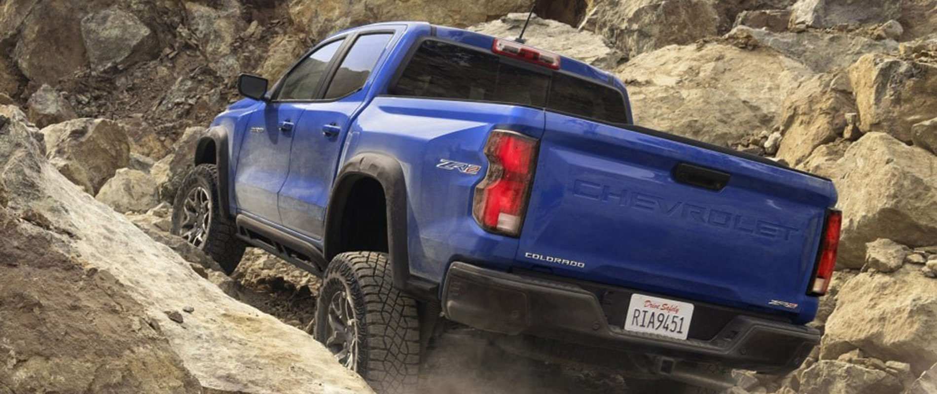 2025 Chevrolet Colorado Trim Comparison Blue Chevy Colorado driving up a rocky, rugged hill