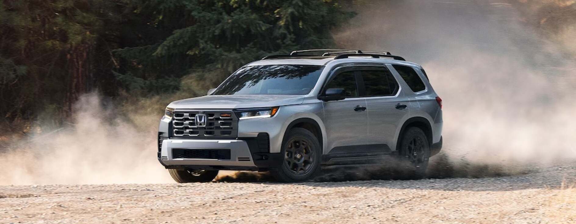 A silver 2026 Honda Pilot SUV driving over bare dirt with dust flying up from the tires