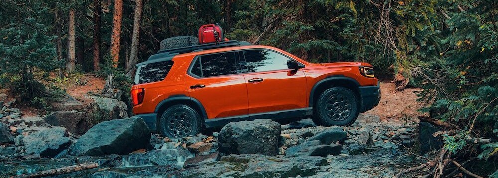 An orange 2026 Honda Passport SUV driving over a rocky river bed