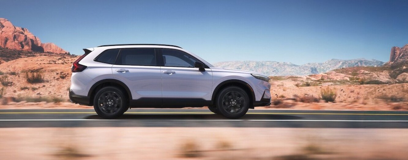 A side view of a light-colored Honda CR-V Hybrid driving down a desert road A side view of a light-colored Honda CR-V Hybrid driving down a desert road