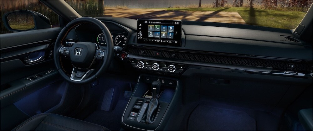 The steering wheel and dashboard of a 2026 Honda CR-V Sport Touring Hybrid, with a body of water visible through the windshield The steering wheel and dashboard of a 2026 Honda CR-V Sport Touring Hybrid, with a body of water visible through the windshield