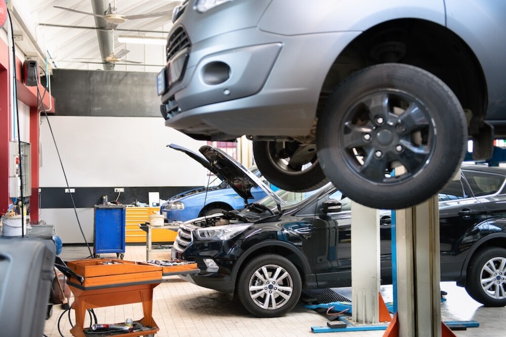 Three cars in a vehicle service center, including one on a hydraulic lift and two more with their hoods open