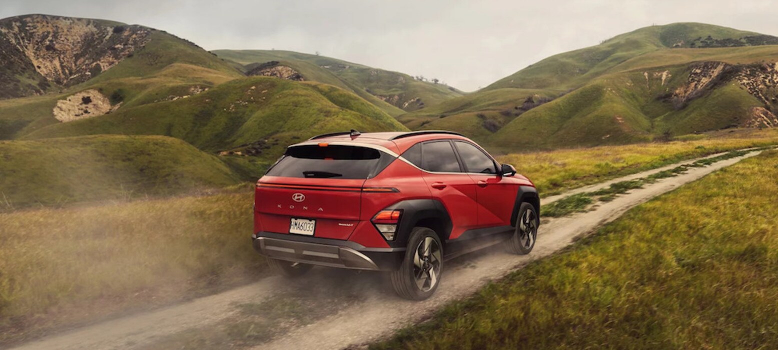 A three-quarters view of a red 2026 Hyundai Kona SUV driving down a mountain trail