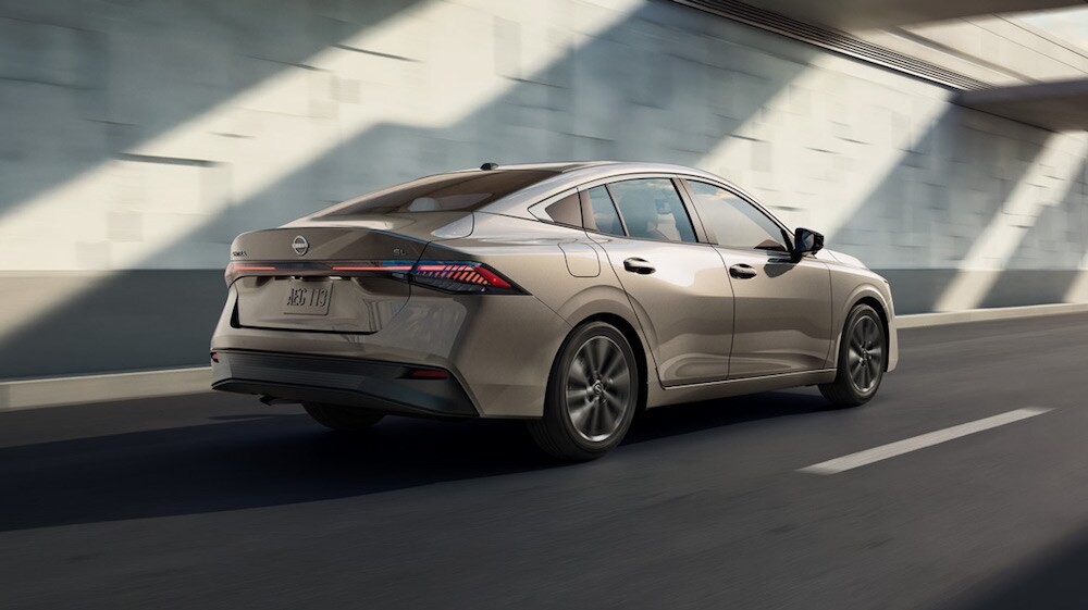 A beige 2026 Nissan Sentra sedan driving past a stone wall A beige 2026 Nissan Sentra sedan driving past a stone wall