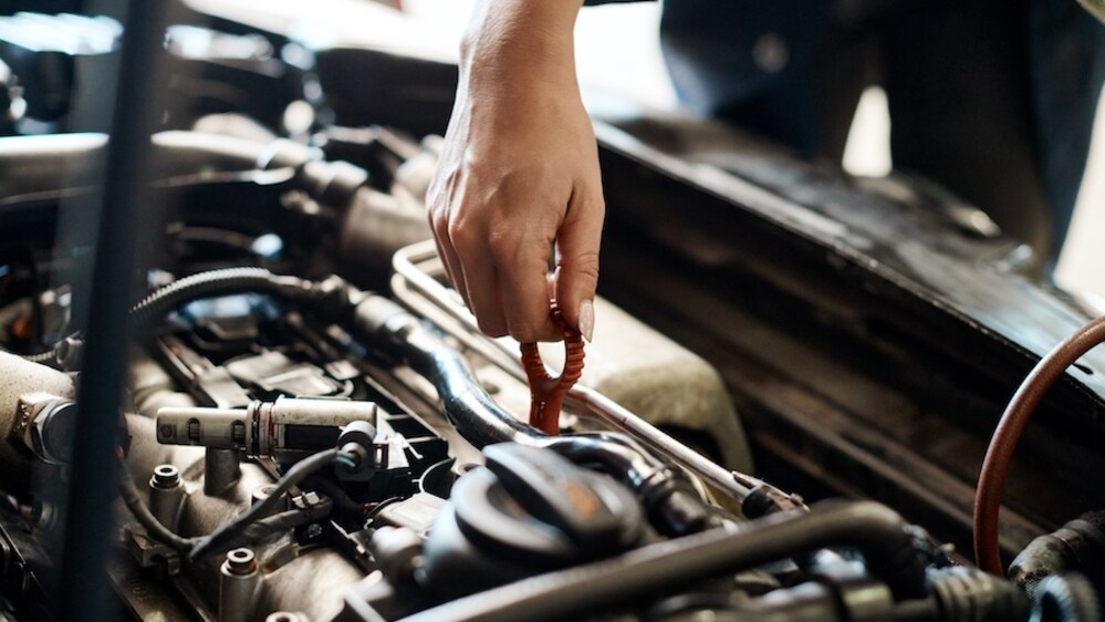 The hand of a white person checking the oil in an open vehicle engine