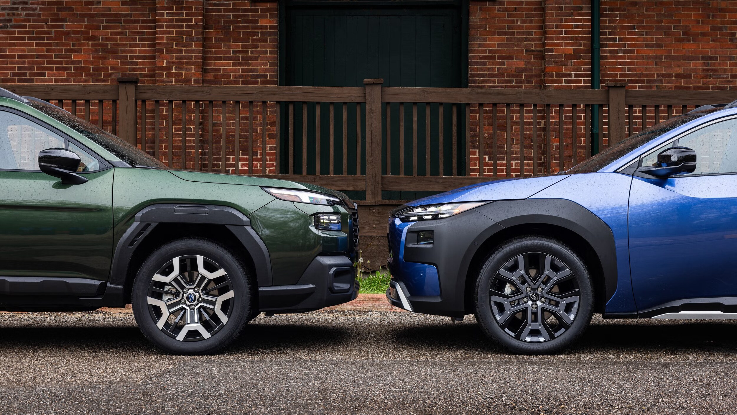 Two Subaru SUVs parked nose-to-nose outside a brick building