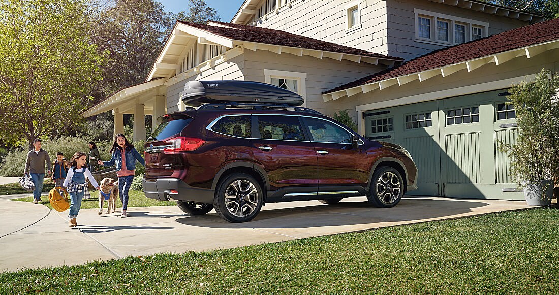 Family walking toward a red Subaru Ascent with a roof cargo box at home