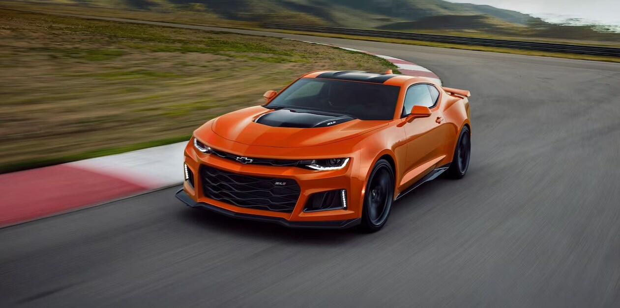 2023-chevy-camaro-3.PNG An overhead view of an orange 2023 Chevy Camaro with black racing stripes on the hood