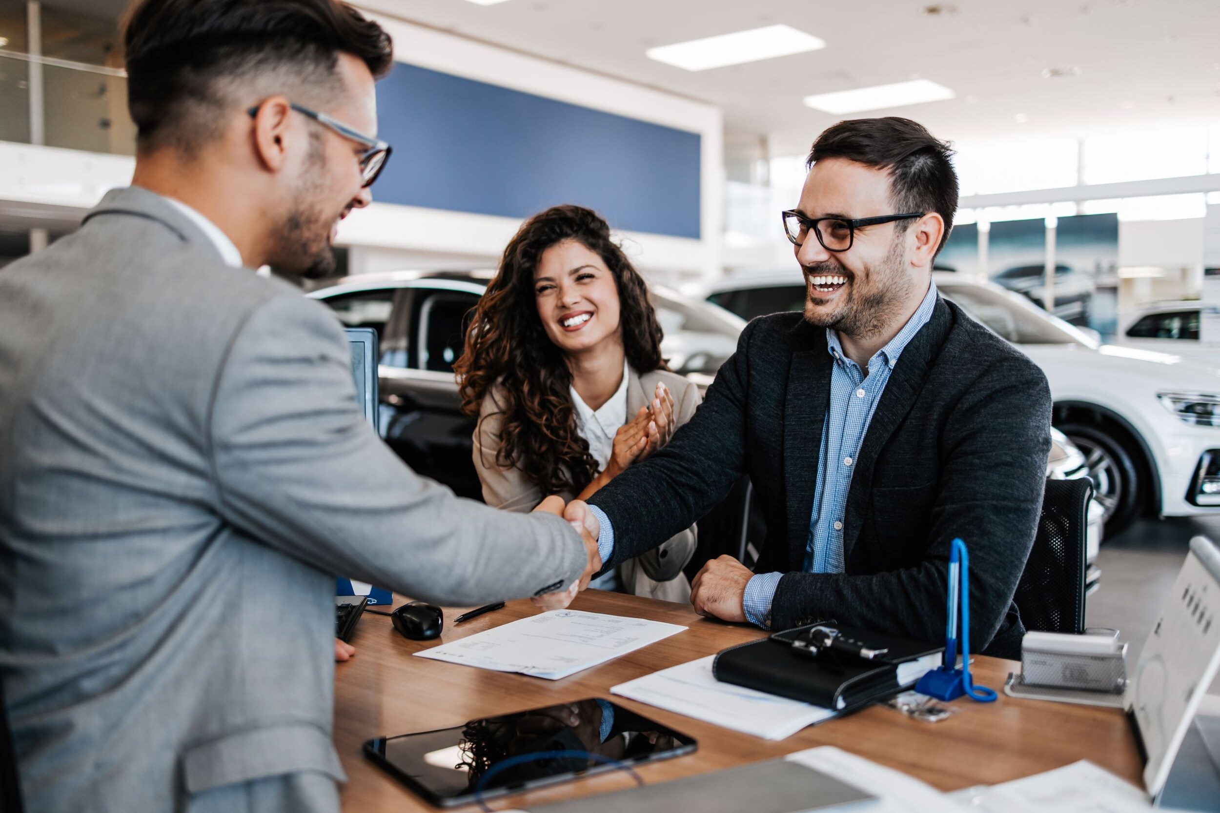 AdobeStock_600538923.jpeg A man shaking hands with a family who just bought a new car.