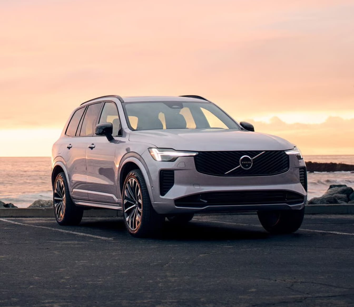 volvo XC90 Plug-In Hybrid parked along the coast with the ocean and a warm sunset in the background.
