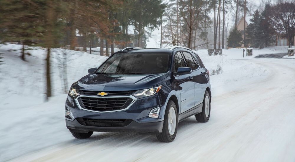 A blue 2018 used Chevy Equinox for sale is shown driving on a snowy path.