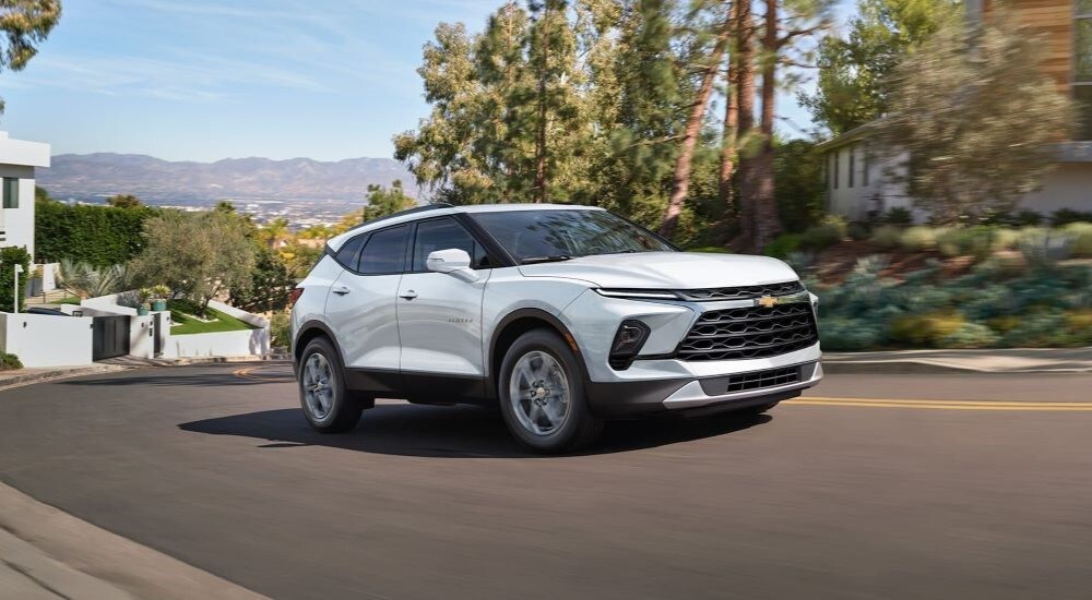 A white 2024 Chevy Blazer is shown driving on a suburban street after looking at Chevy SUVs for …