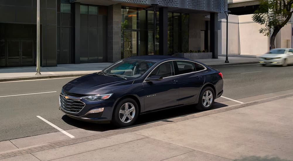 A dark blue 2023 Chevy Malibu is shown parked on a city street after leaving a Chevy dealer in …