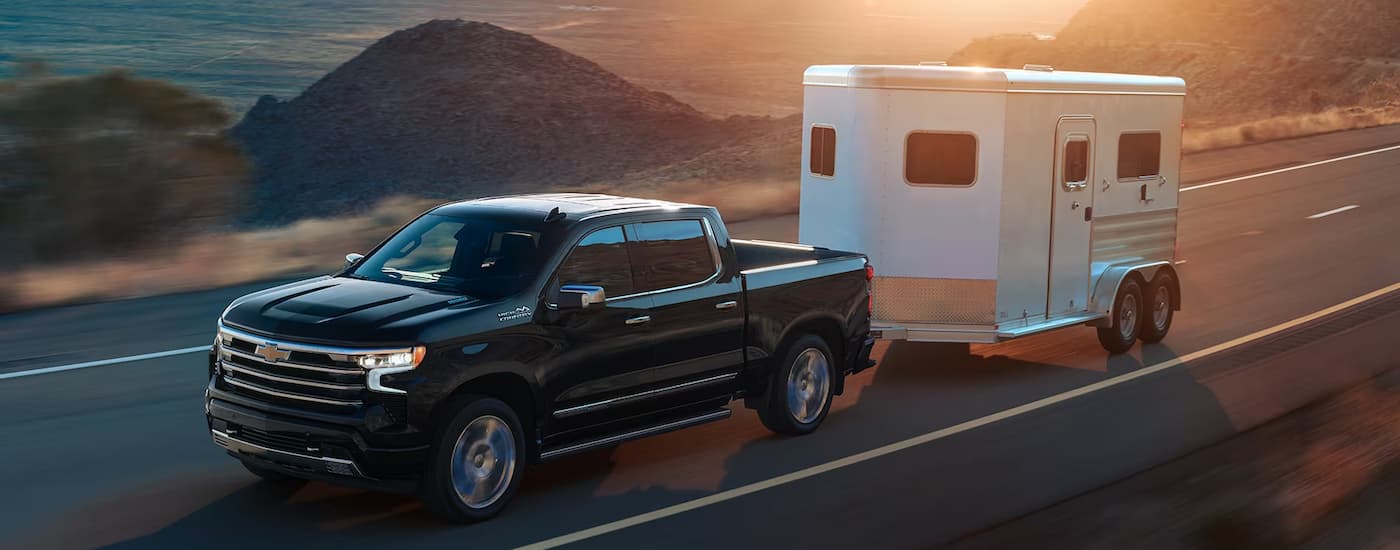 Chevy%20Silverado%201500%20for%20sale%20in%20Columbus%20-%202024%20Chevy%20Silverado%201500%20High%20Country%20-%20Black%20Towing.jpg A black 2024 Chevy Silverado 1500 High Country is towing a trailer on an open road.