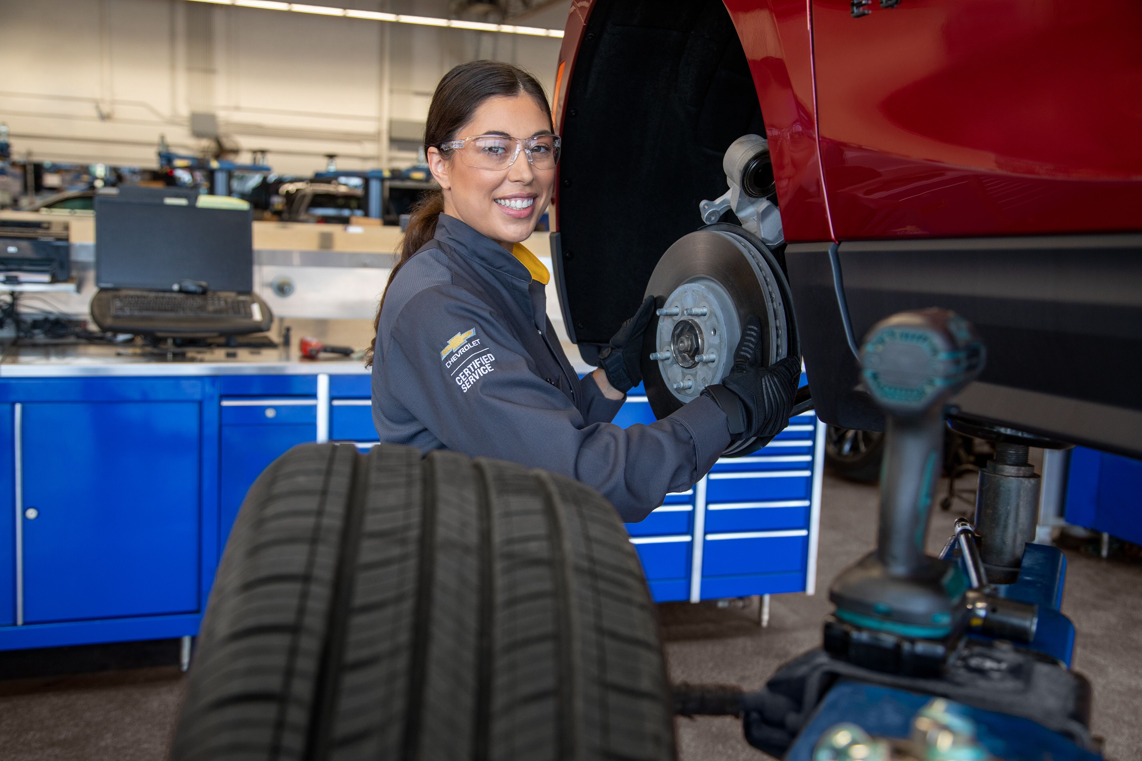 Chevy Maintenance Smiling female Chevrolet certified service technician working on brake rotor assembly and wheel hub.
