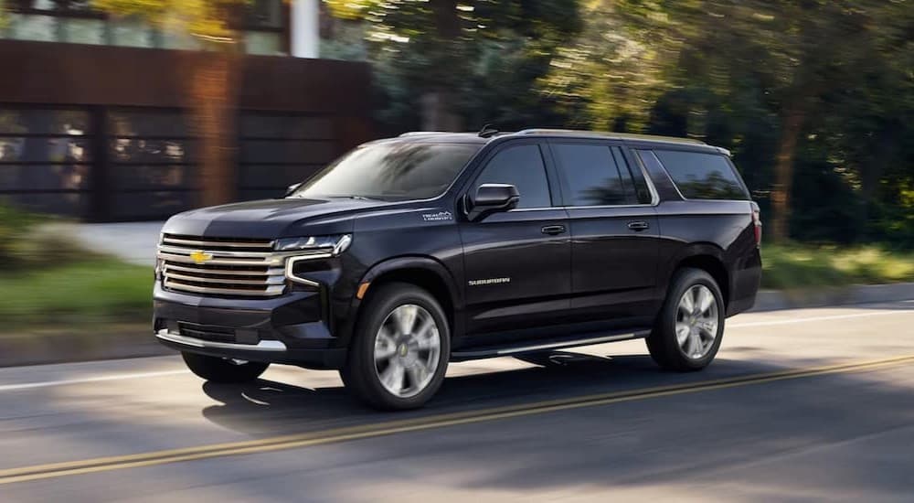 2024%20chevy%20suburban%20high%20country%20-%20black.jpg A blue 2024 Chevy Suburban High Country is shown driving near a house.