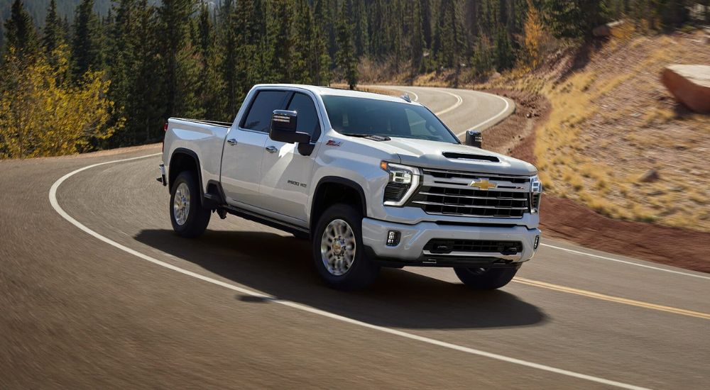 A white 2024 Chevy Silverado 2500 for sale is shown is shown driving on a winding road.