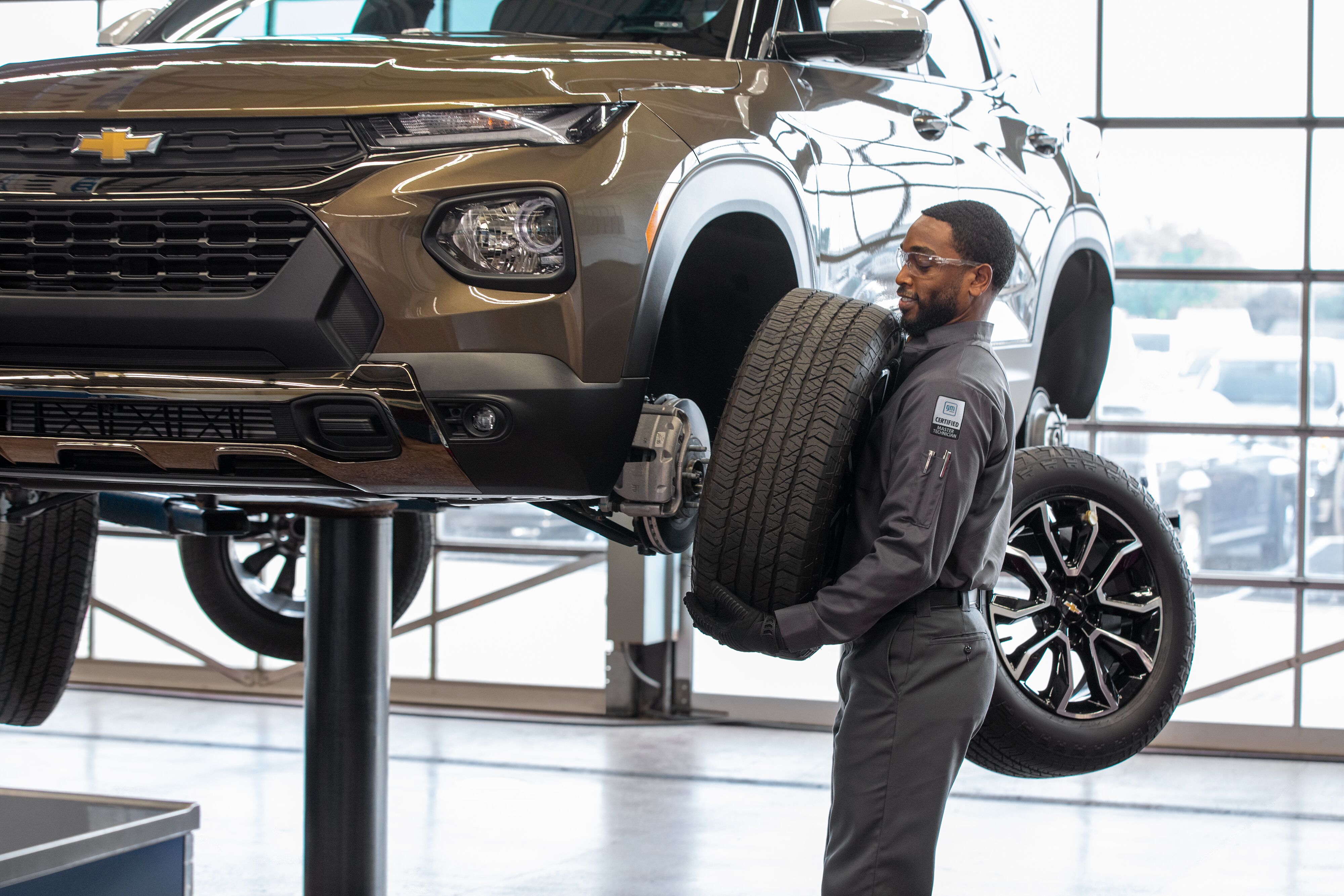 Chevy Maintenance GM certified technician installing a new wheel and tire onto an elevated bronze Chevrolet SUV in the service bay.