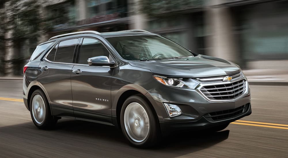 A grey used 2019 Chevy Equinox for sale is shown driving on a winding road.