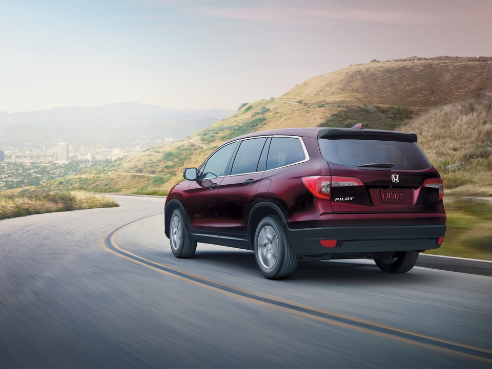 2020-Honda-Pilot-LX-SUV-L01.png dark red Honda Pilot SUV driving on a hill-covered highway