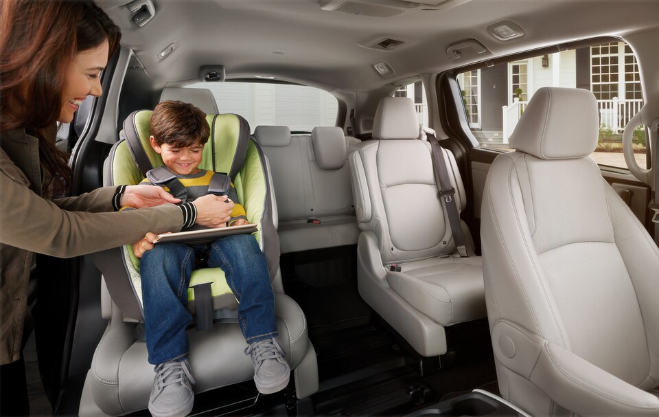 2022-Honda-Odyssey-Elite-Van-I01.png tan interior Honda Odyssey minivan with driver buckling a child into a second row captain's chair